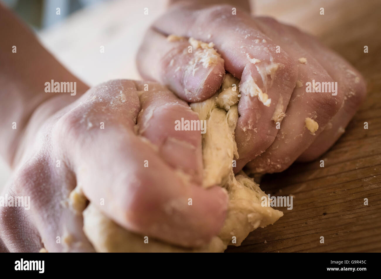 Close-up di due forti mani di un fornaio che sono manualmente gli impasti su una ruvida, cucina in legno tabella Foto Stock