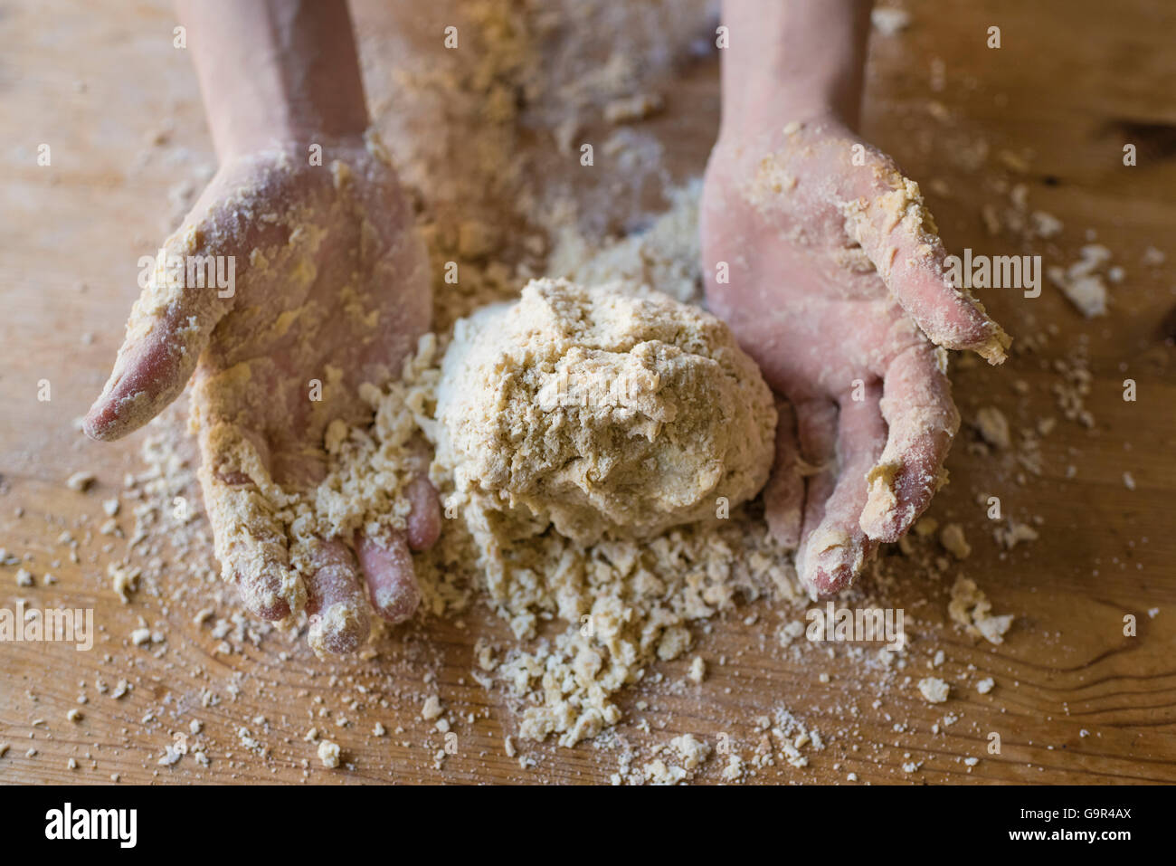 Close-up di due forti mani di un fornaio che sono manualmente gli impasti su una ruvida, cucina in legno tabella Foto Stock
