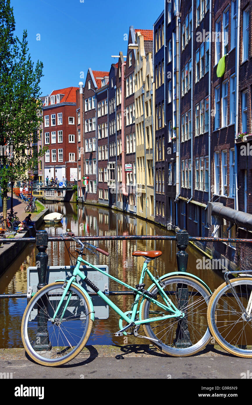 Biciclette su un ponte su Oudezijds Achterburgwal canal e case di Amsterdam, Olanda Foto Stock