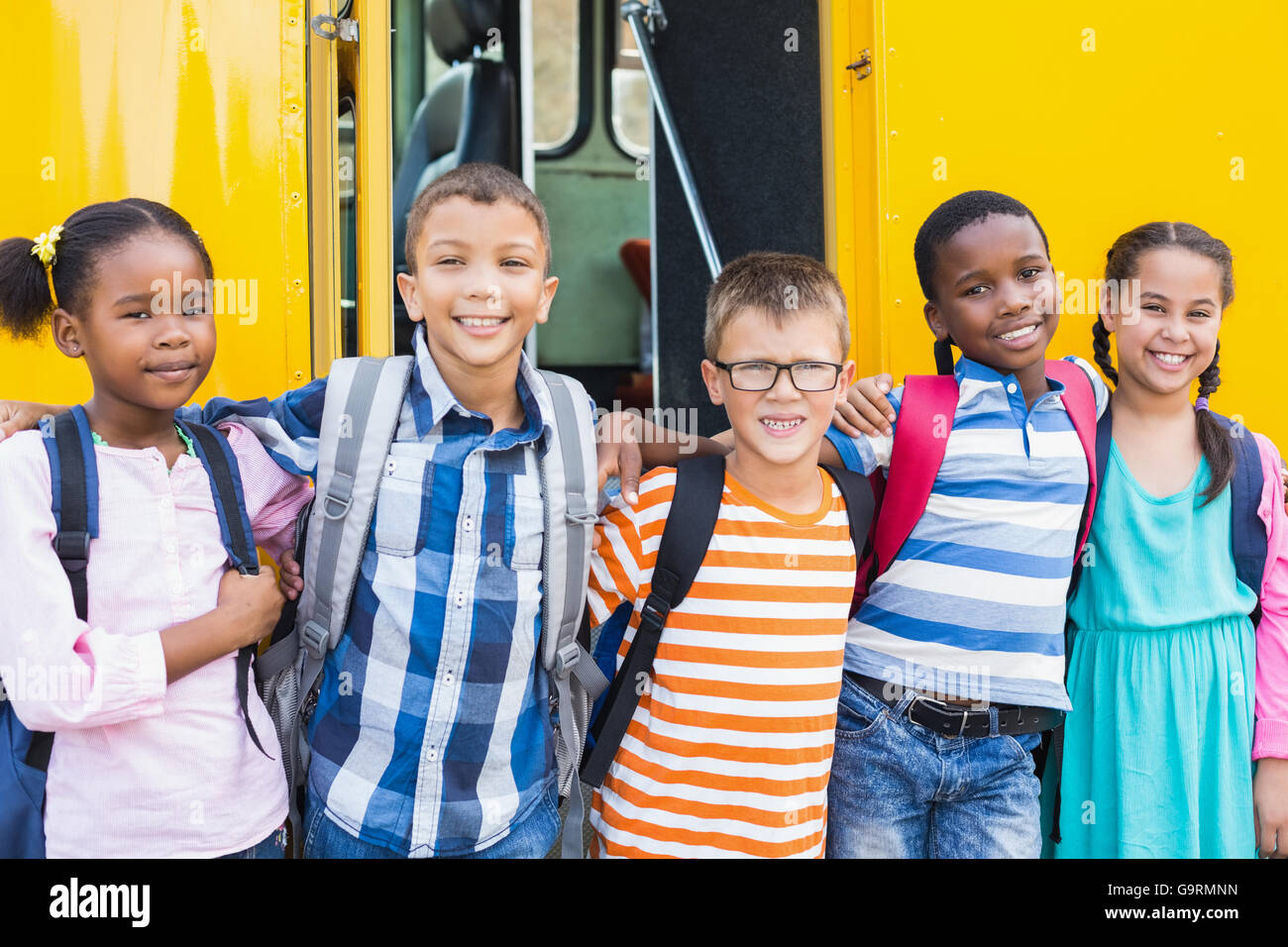 Bambini sorridenti in piedi intorno al braccio nella parte anteriore del bus di scuola Foto Stock
