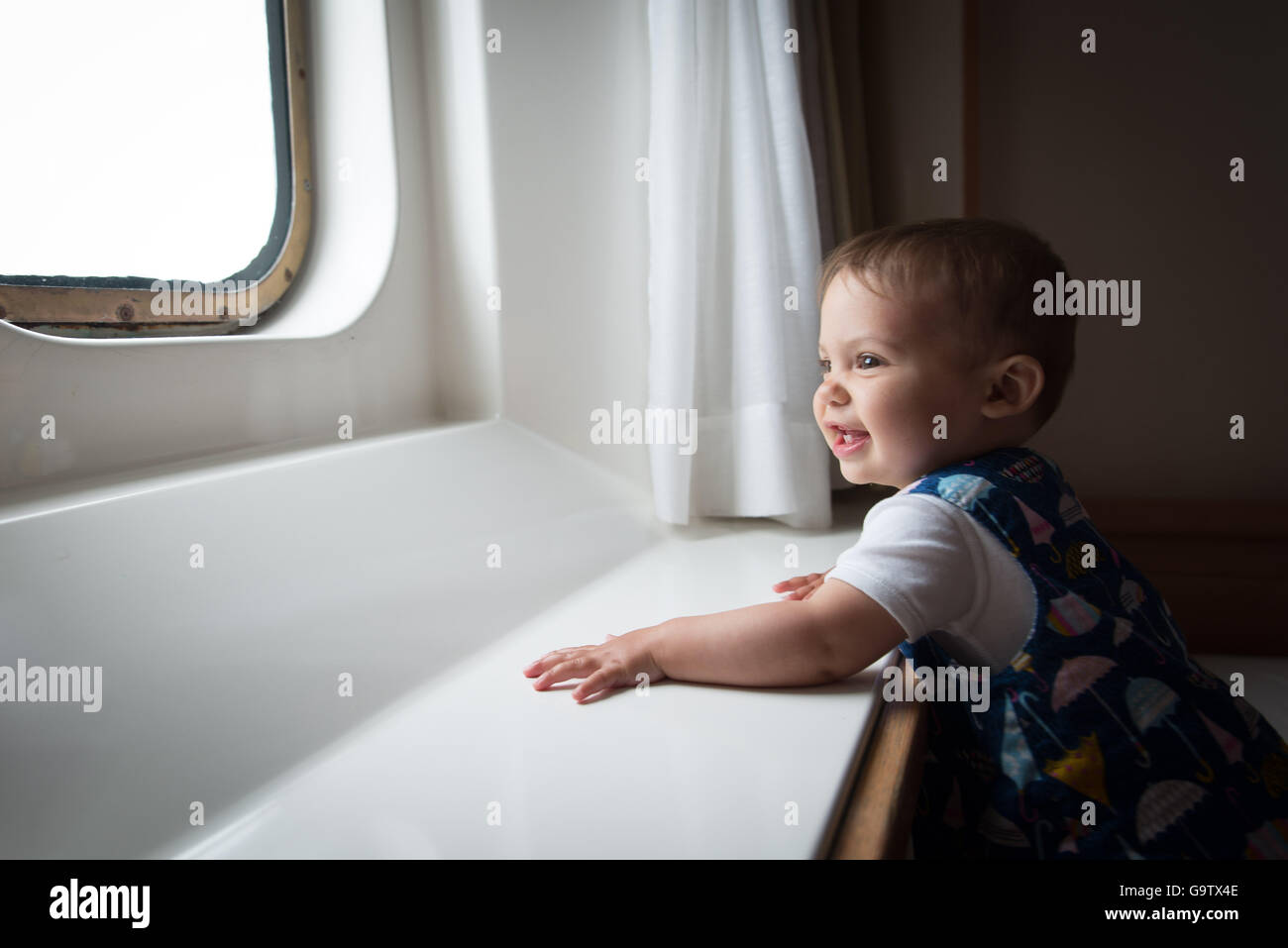 Baby guardando fuori da una finestra ad oblò a bordo di un traghetto Foto Stock