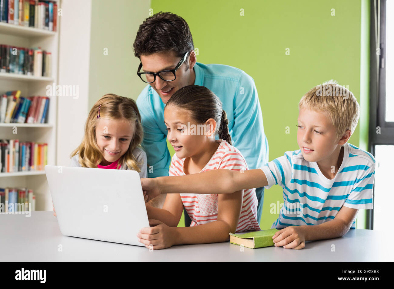 Insegnanti e bambini usando computer portatile in biblioteca Foto Stock
