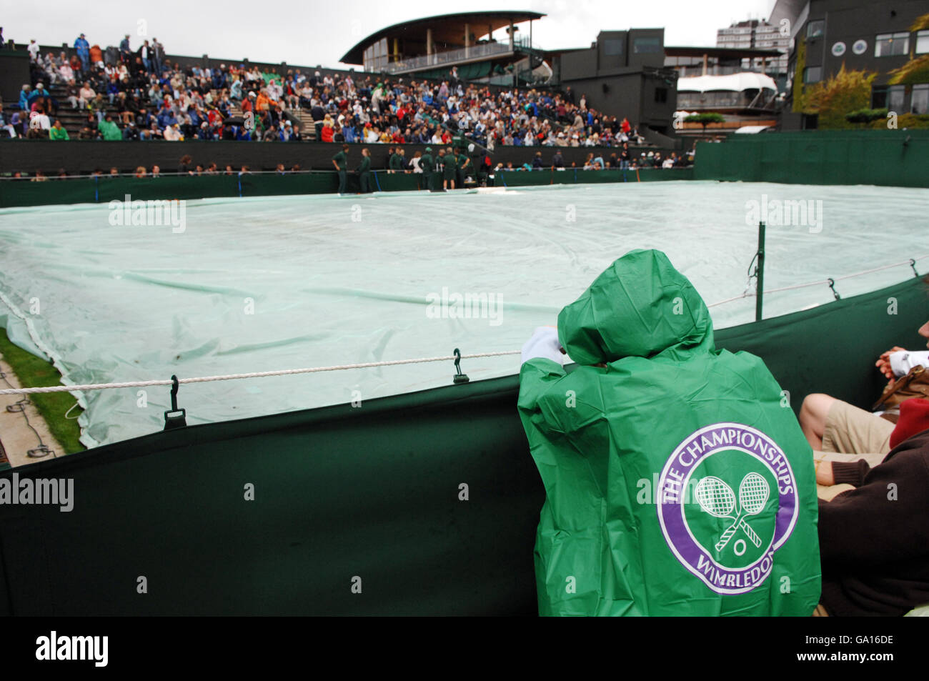 Un fan attende che i ritardi della pioggia si svolgano durante il campionato di tennis All England Lawn a Wimbledon. Foto Stock