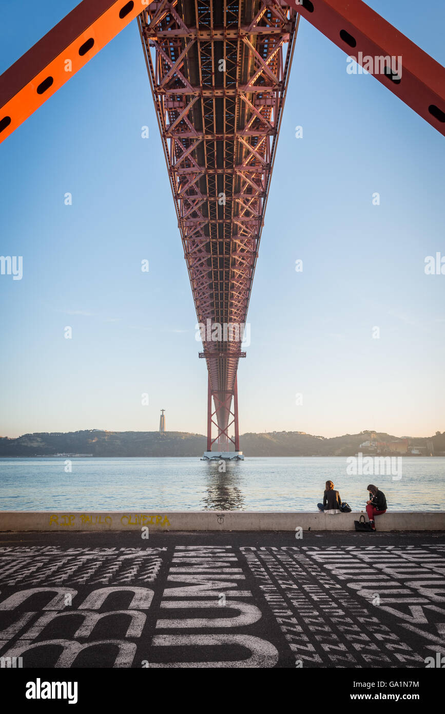Un turista seduto sotto il XXV Aprile del ponte a Lisbona Foto Stock