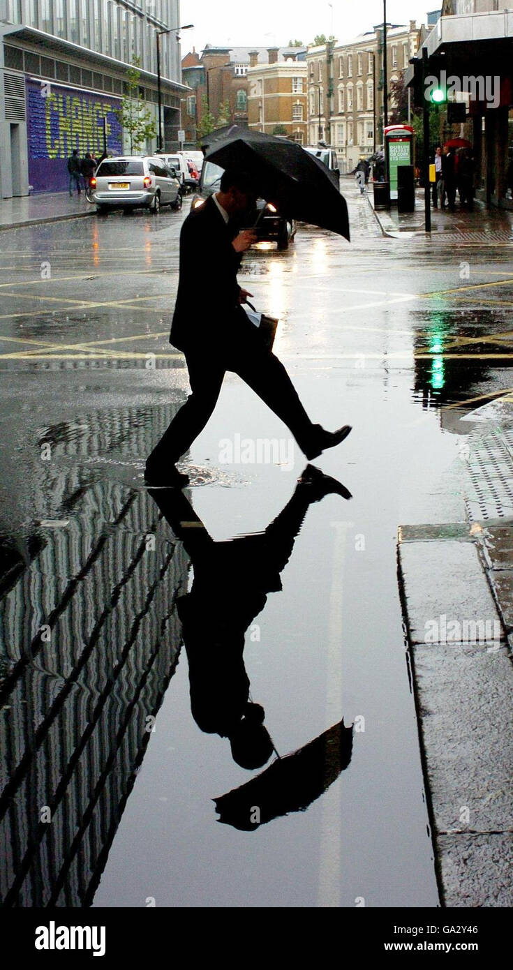 Un uomo si affaccia su una pozza sul lato di una strada londinese, dopo pesanti docce. Foto Stock