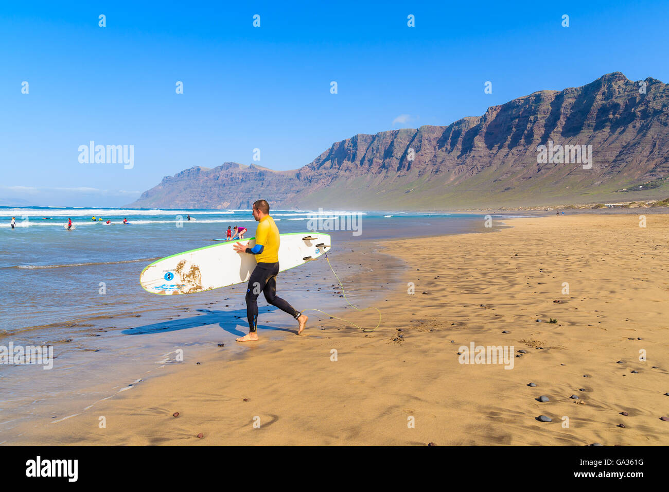 Spiaggia di Famara, Lanzarote Island - Jan 15, 2015: uomo correre con la tavola da surf sulla spiaggia di Famara. Questo è famoso posto sulla isola di Lanzarote per fare surf a causa di forti venti. Foto Stock