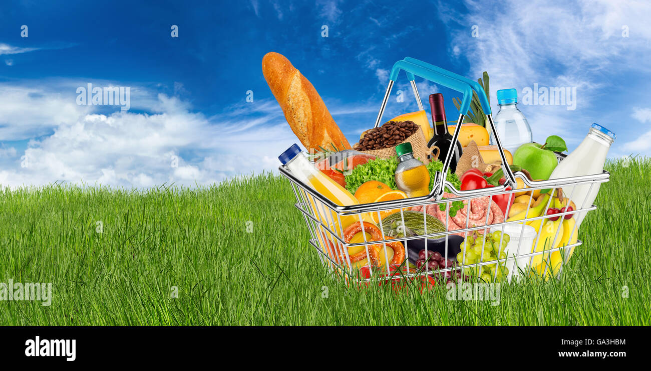 Carrello riempito con cibo sul prato di fronte cielo blu Foto Stock