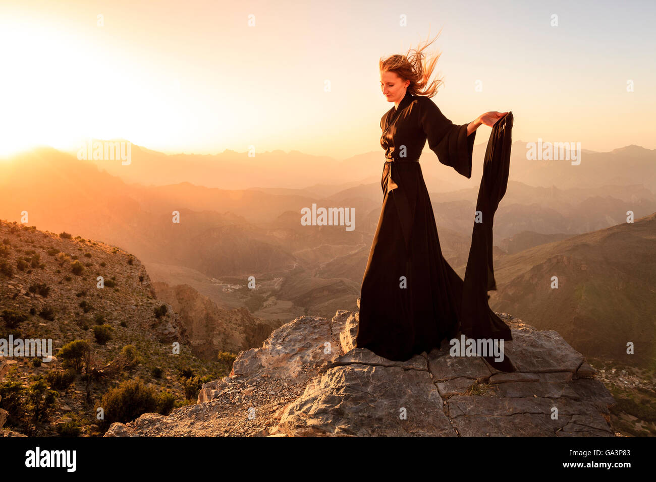 Lone donna in abaya in Al montagne Hajar di Oman al tramonto Foto Stock