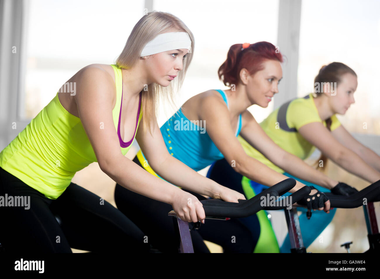 La pratica di fitness, gruppo di montare tre femmine bellissime escursioni in bicicletta in sports club, facendo esercizi cardio per dimagrire in classe Foto Stock