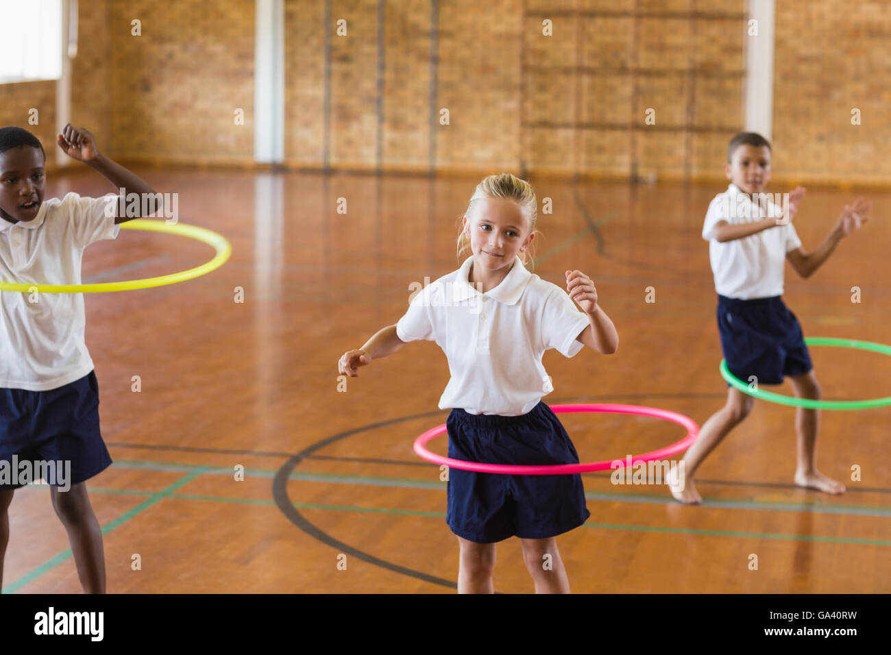 Gli studenti a giocare con hula hoop nella palestra della scuola Foto Stock