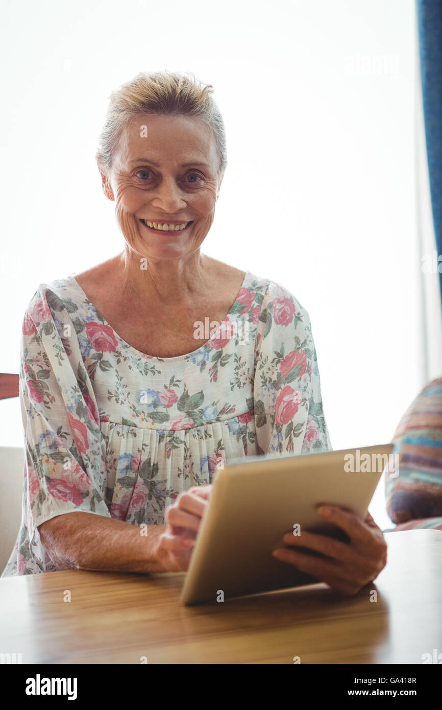 Senior donna guardando la telecamera utilizzando una tavoletta digitale Foto Stock