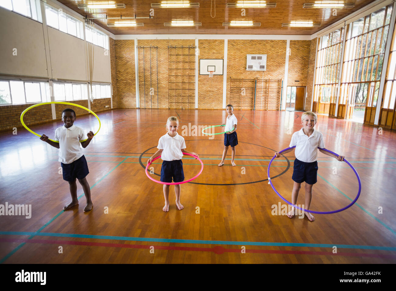Gli studenti a giocare con hula hoop nella palestra della scuola Foto Stock