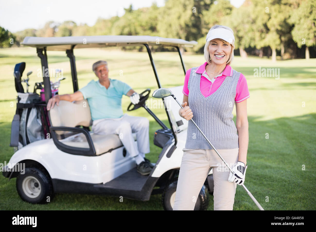 Sorridente donna matura in piedi da uomo in golf buggy Foto Stock