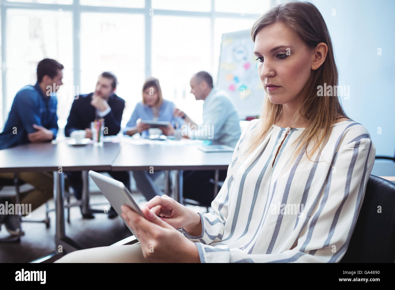 Imprenditrice utilizzando digitale compressa contro i colleghi nella sala riunioni Foto Stock