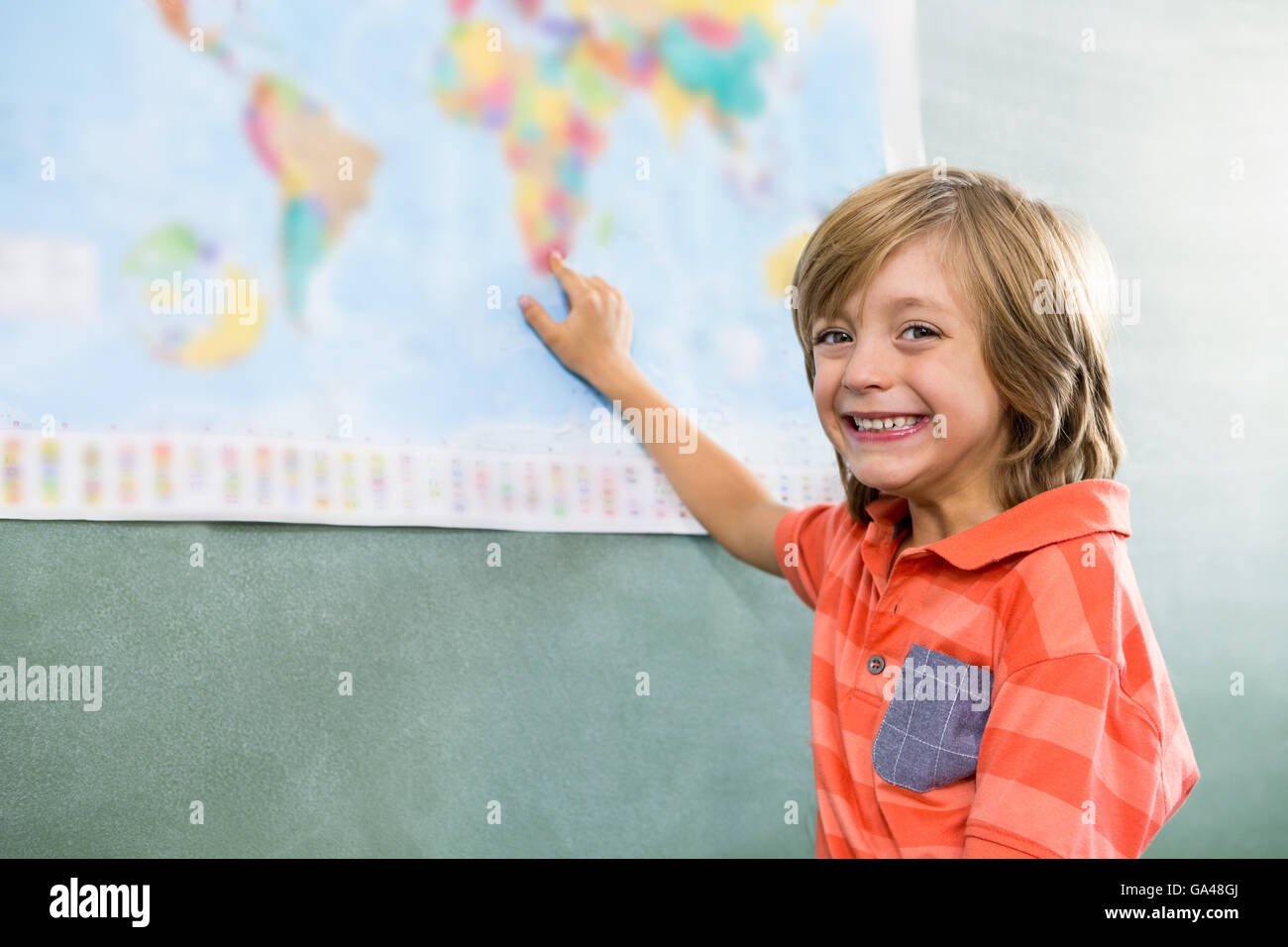 Felice ragazzo puntando sulla mappa in aula Foto Stock