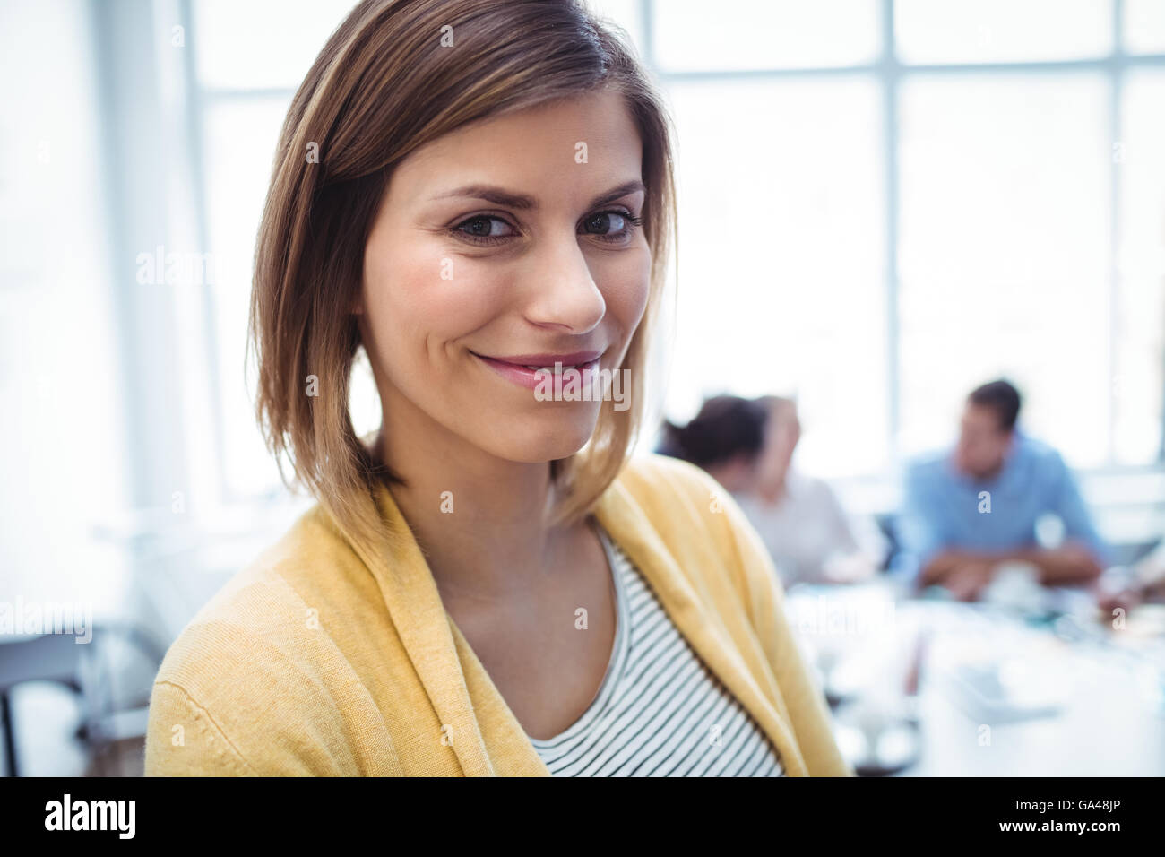 Imprenditrice sorridente in piedi contro i colleghi Foto Stock