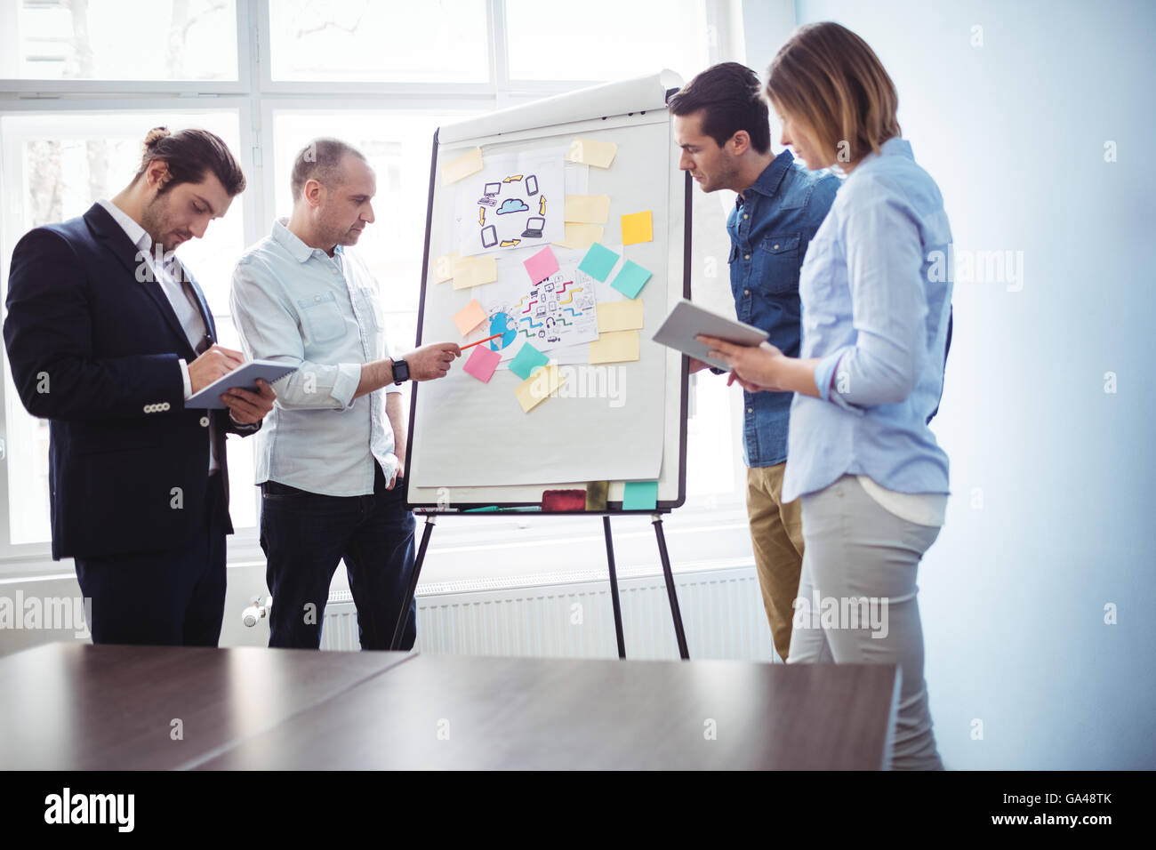 I colleghi discutendo in sala riunioni utilizzando una lavagna bianca Foto Stock