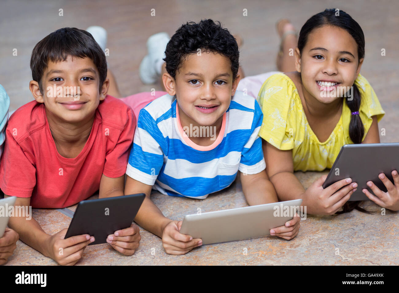 I bambini utilizzando le compresse digitale mentre giaceva sul pavimento Foto Stock
