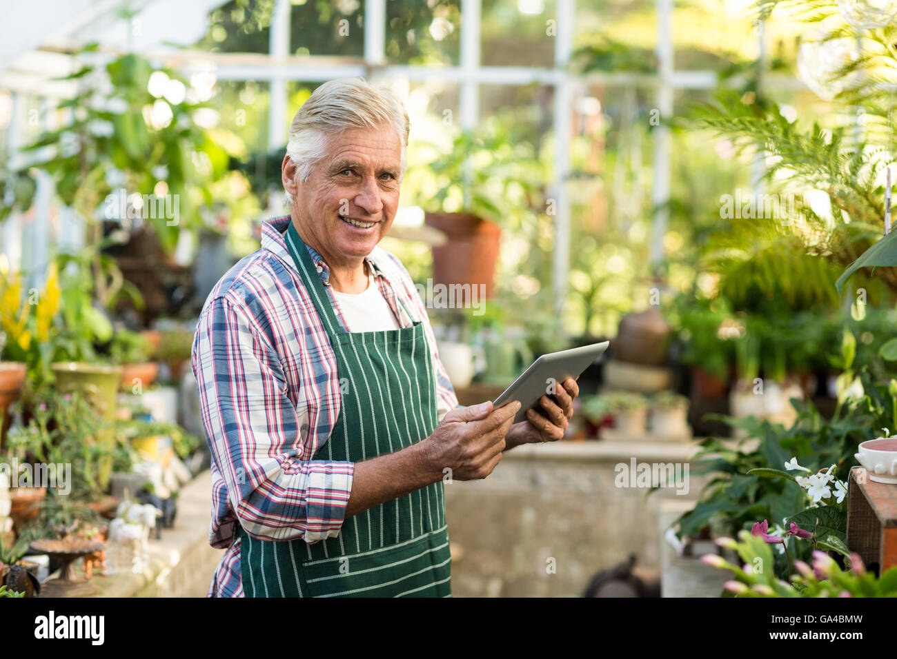 Giardiniere maschio sorridere mentre usando tavoletta digitale Foto Stock