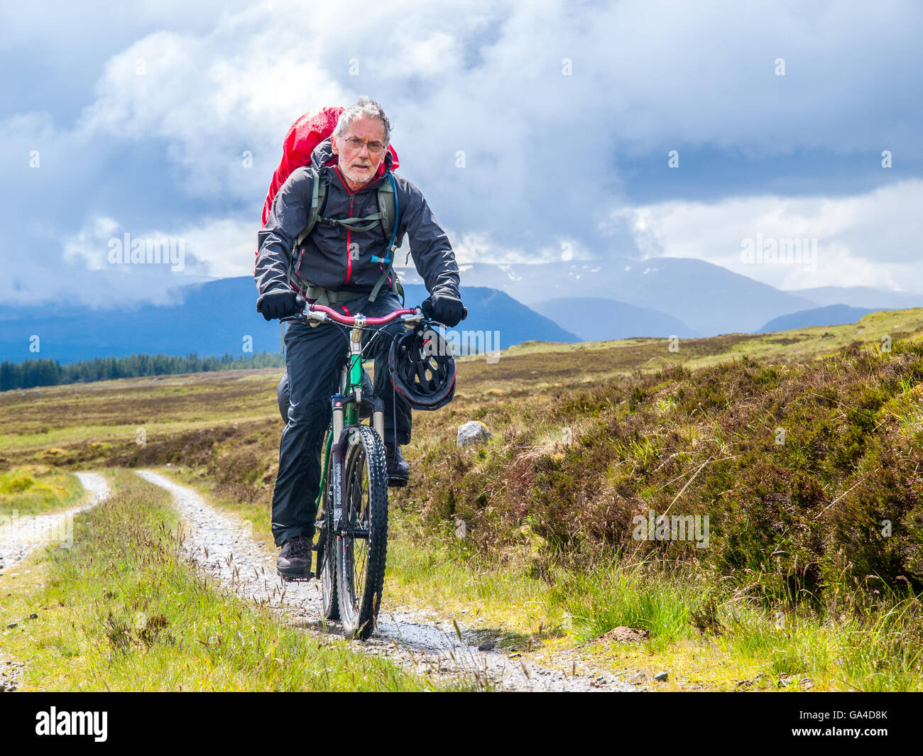 Uomo in pensione su una bici da corsa di imballaggio attraverso le Highlands scozzesi Foto Stock