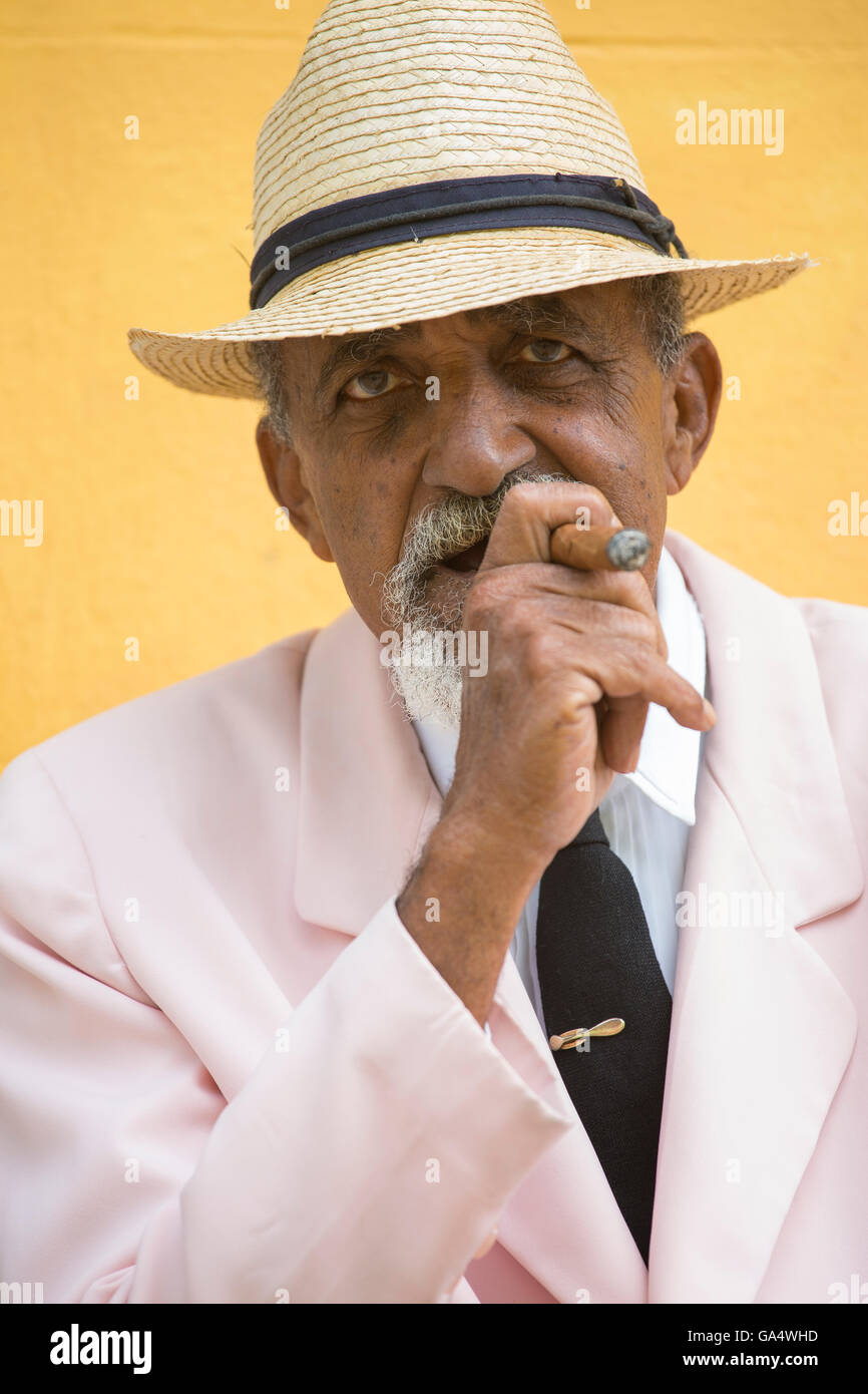 Ben vestito gentleman cubano in rosa blazer con cravatta seduti all'aperto di fumare un sigaro, Plaza Major, Trinidad, Cuba, Caraibi Foto Stock