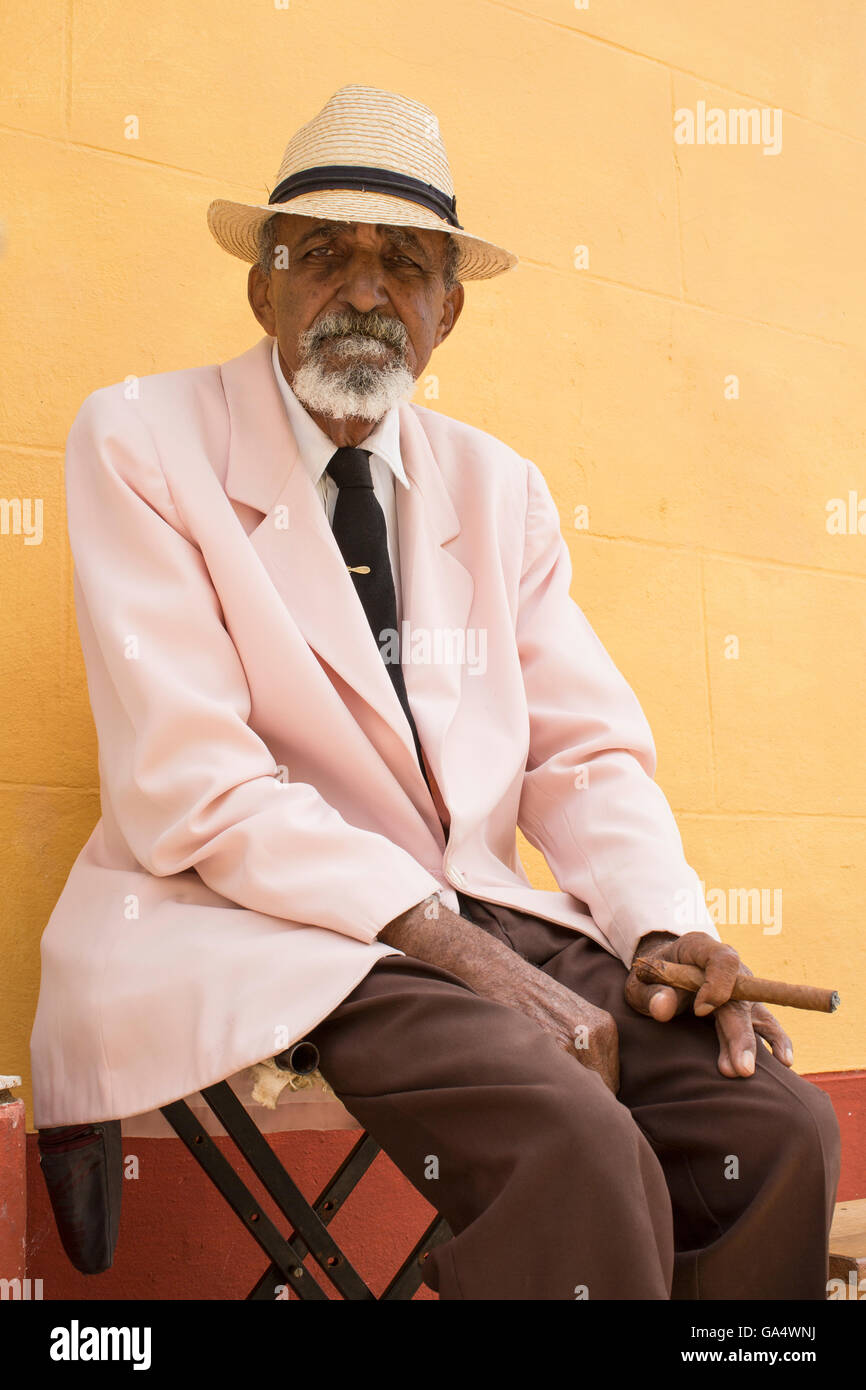 Uomo locale in hat con sigaro seduti su uno sgabello vicino a Plaza Major, Trinidad, Cuba Foto Stock