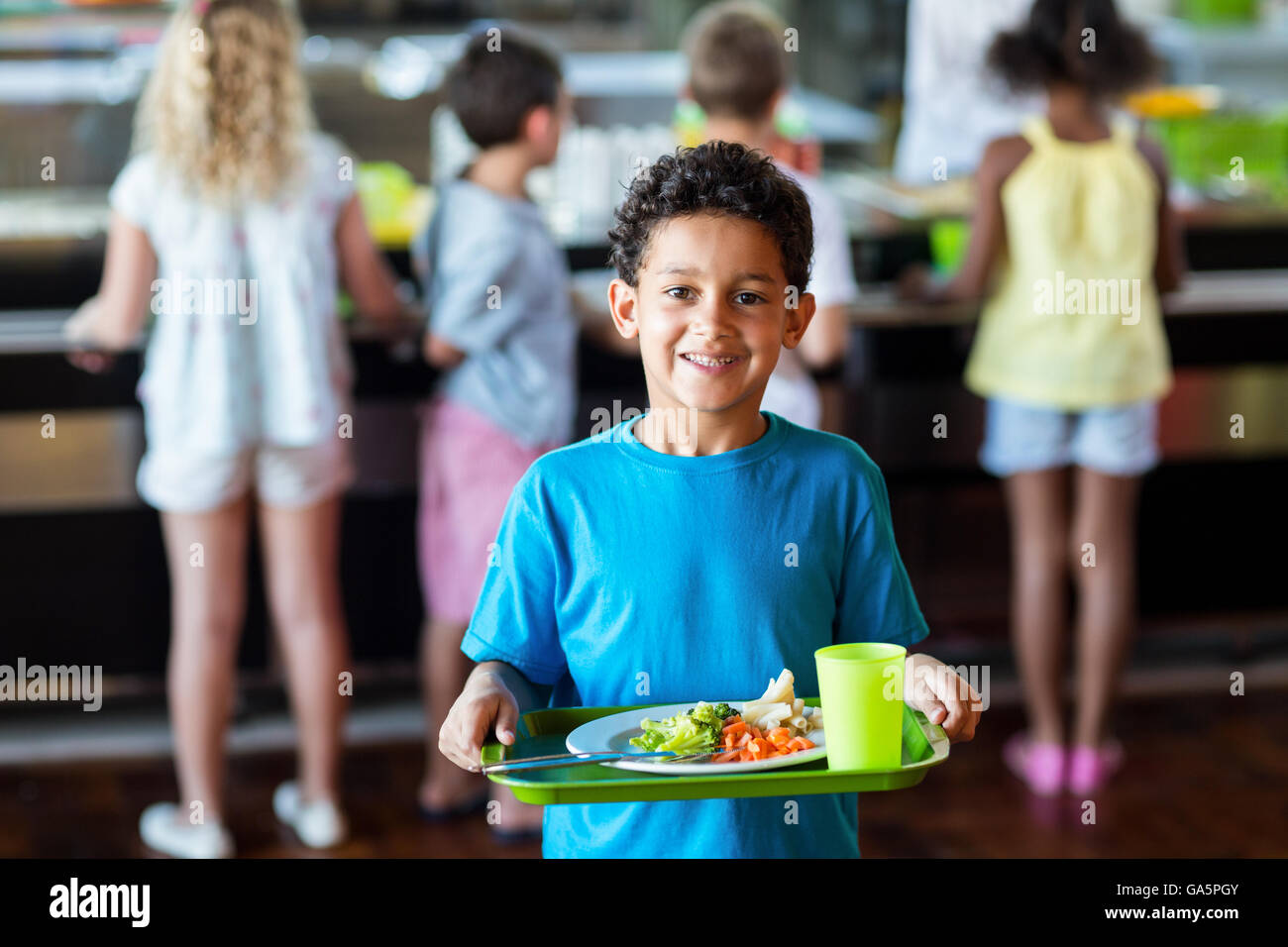 Felice schoolboy tenendo il vassoio per alimenti in mensa Foto Stock