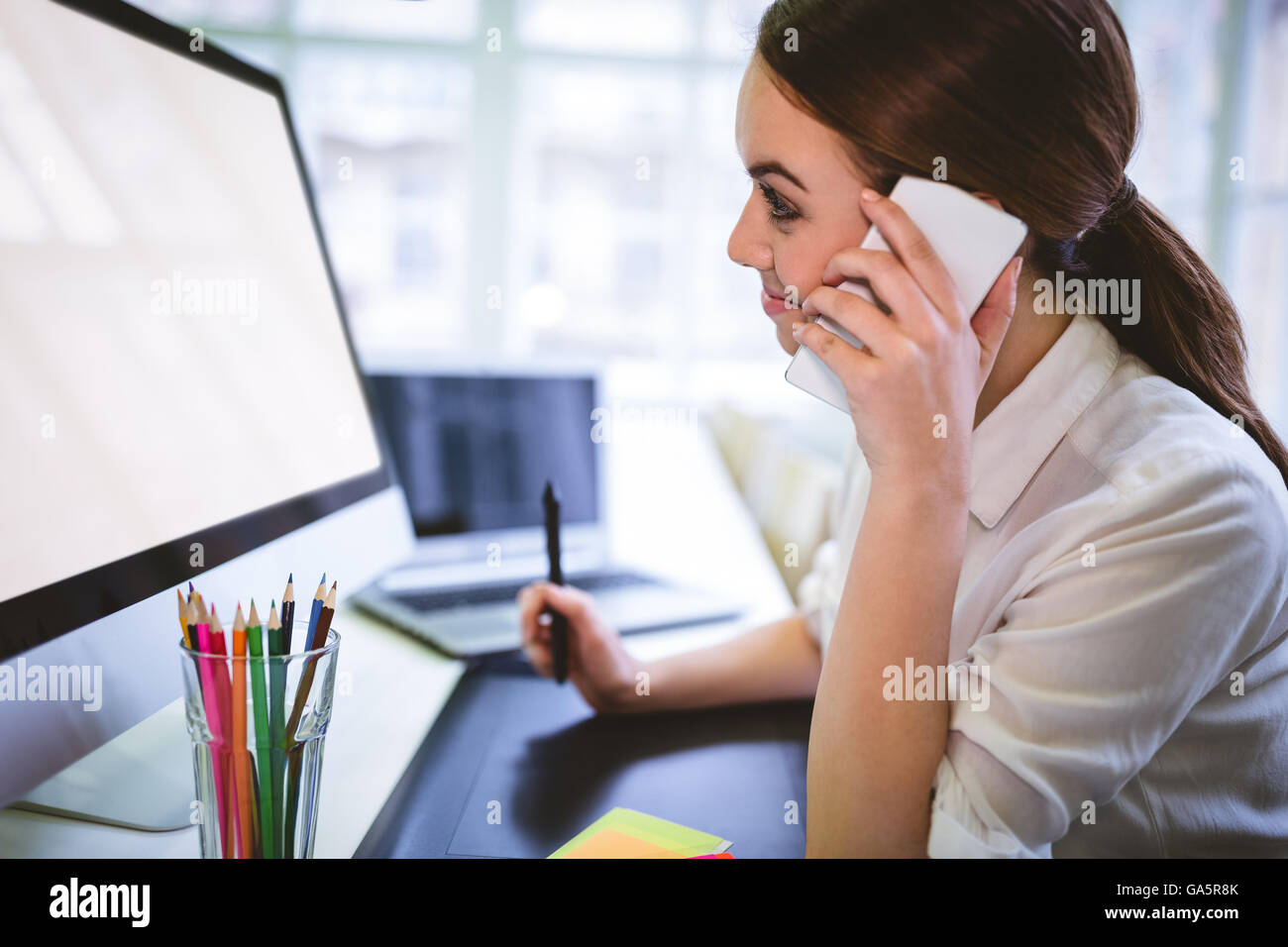 Donna sorridente graphic designer parlando al telefono alla scrivania Foto Stock