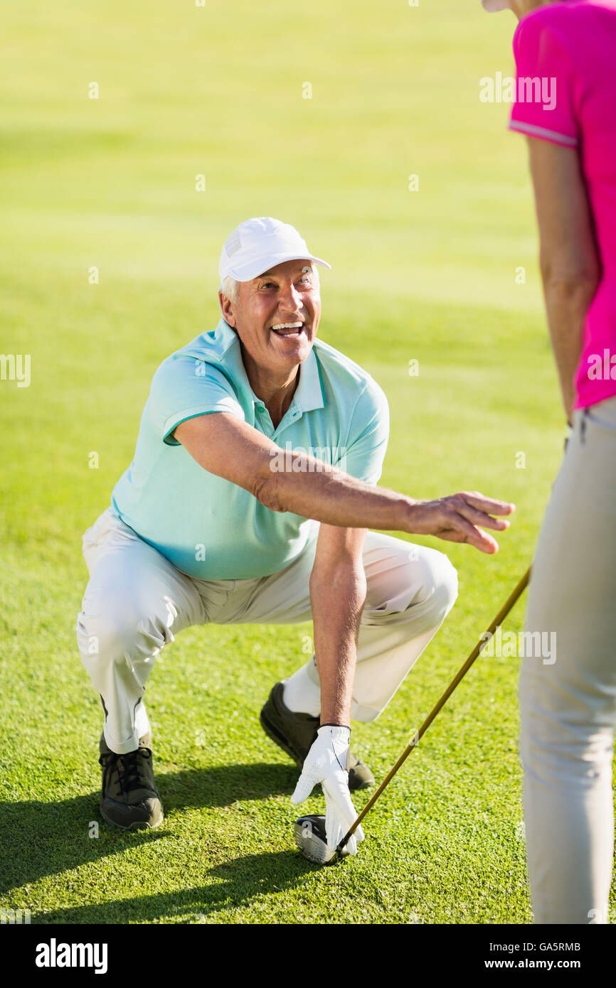 Sorridente golfista maturo uomo accovacciato mentre l'insegnamento donna Foto Stock