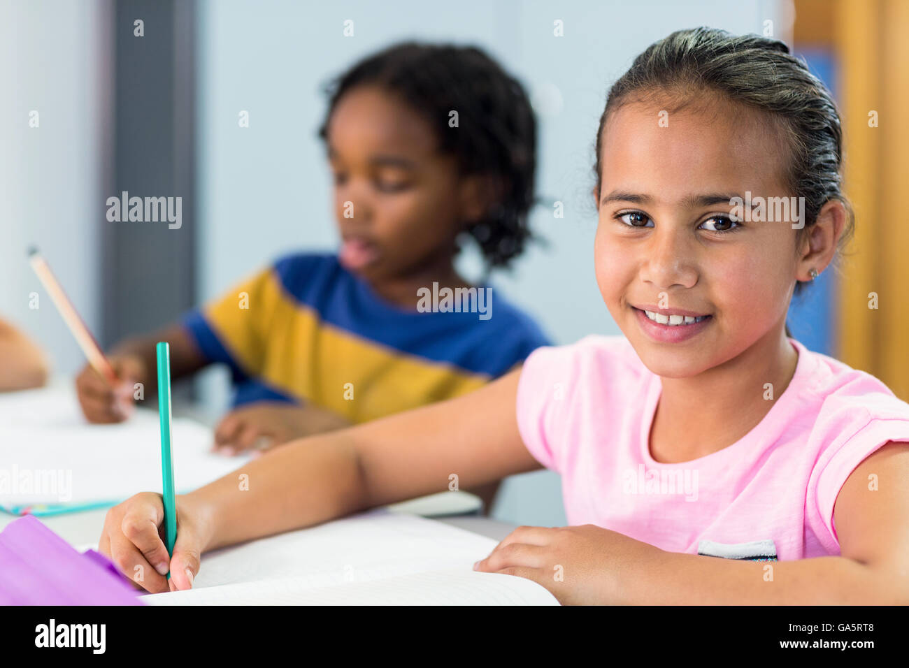 La scolaretta sorridente con un compagno di classe scritta sul libro Foto Stock