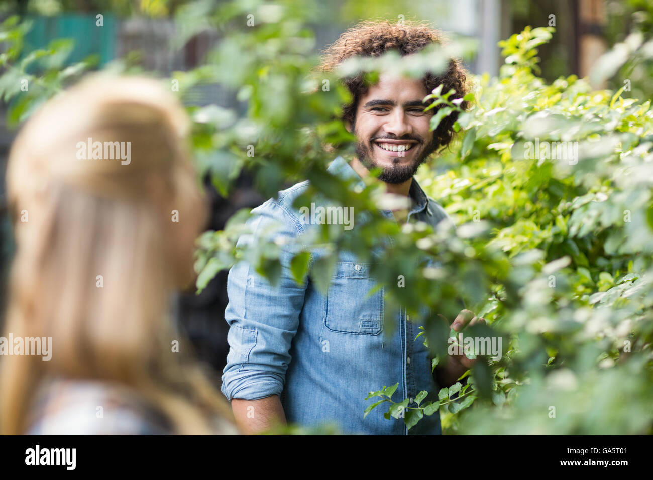 Giardiniere maschio guardando donna in piedi dalle piante Foto Stock