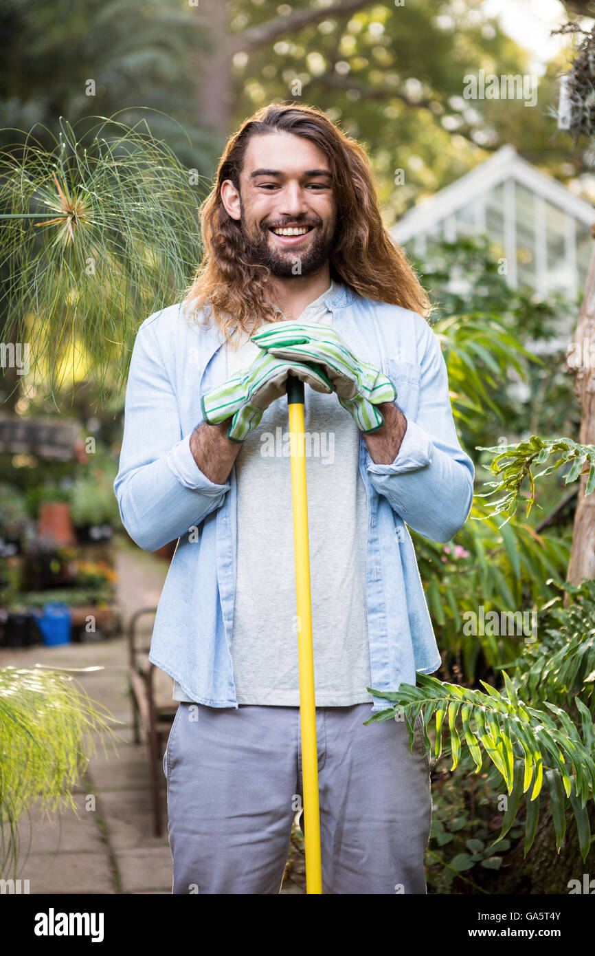 Ritratto di felice giardiniere con capelli lunghi tenendo l'attrezzo in giardino Foto Stock