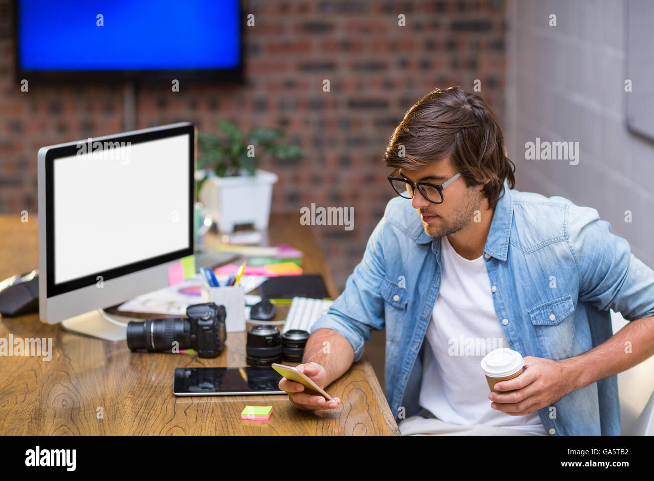 Uomo con tazza monouso tramite cellulare in ufficio Foto Stock