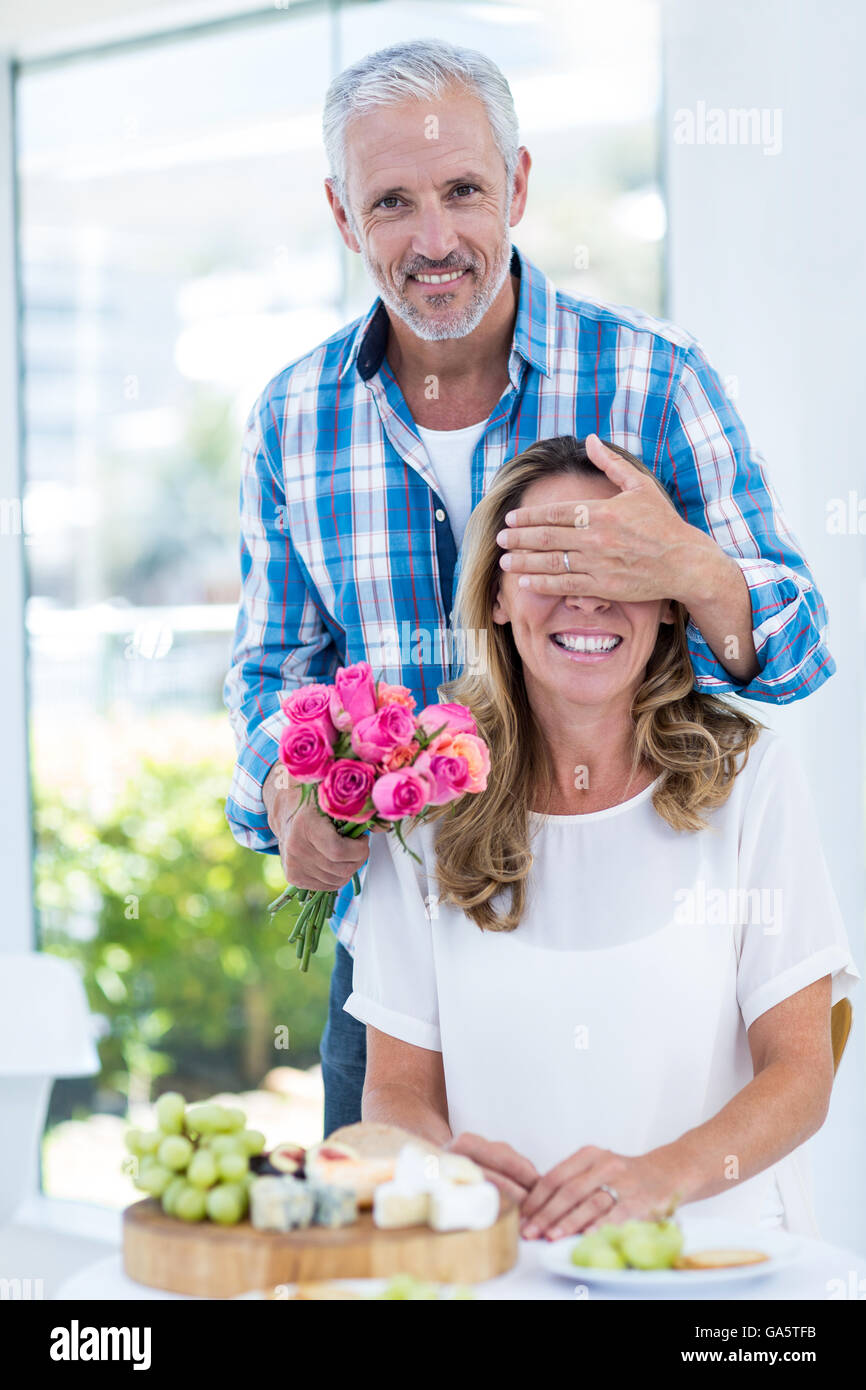 Uomo che copre gli occhi della moglie mentre dà le rose Foto Stock