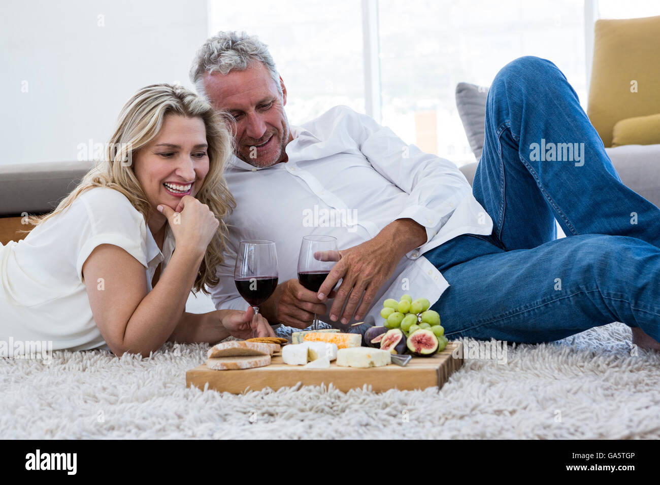 Coppia felice con il vino rosso e il cibo mentre giaceva sul tappeto Foto Stock