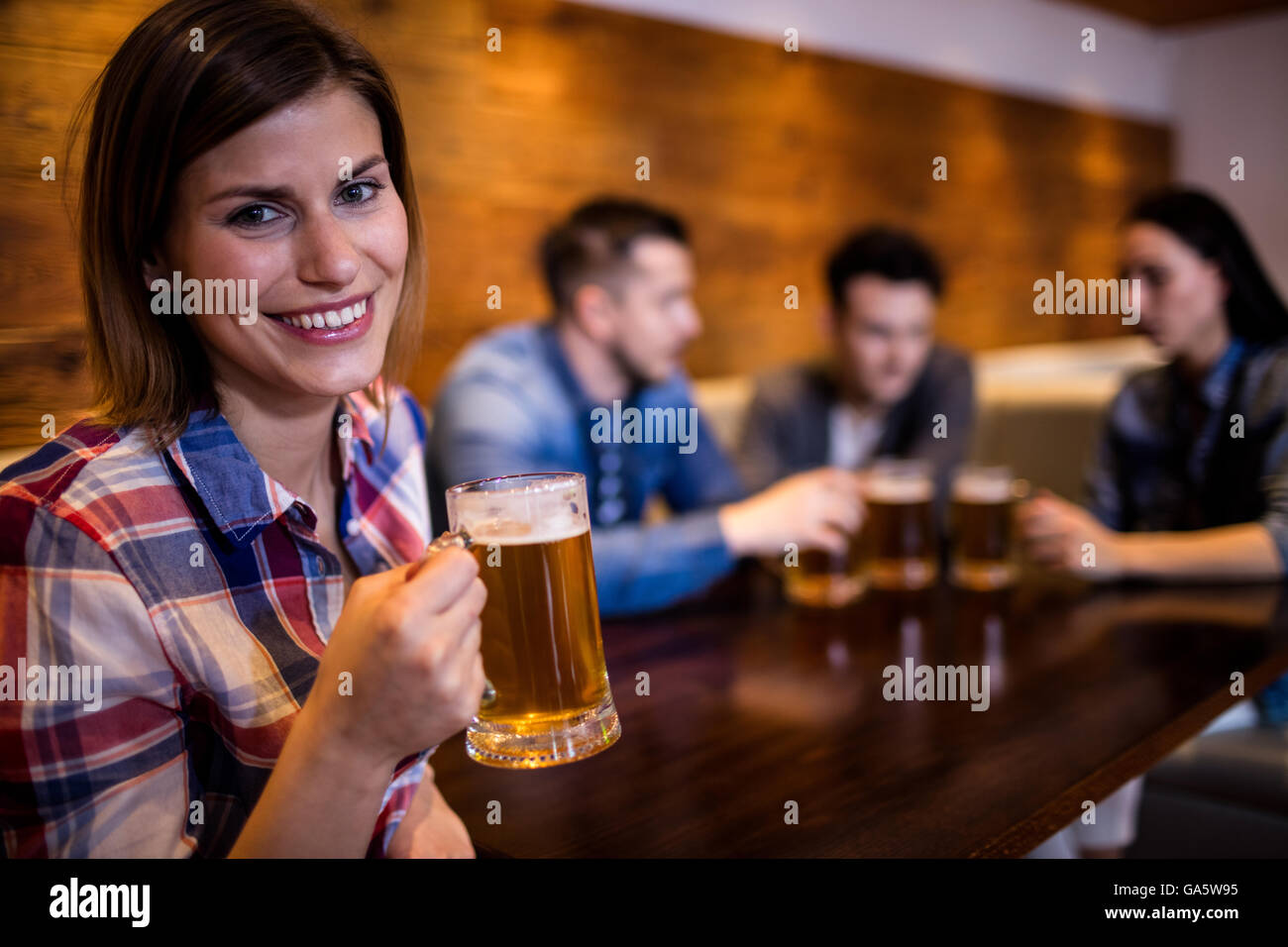 Donna che mantiene boccale di birra mentre gli amici in background Foto Stock