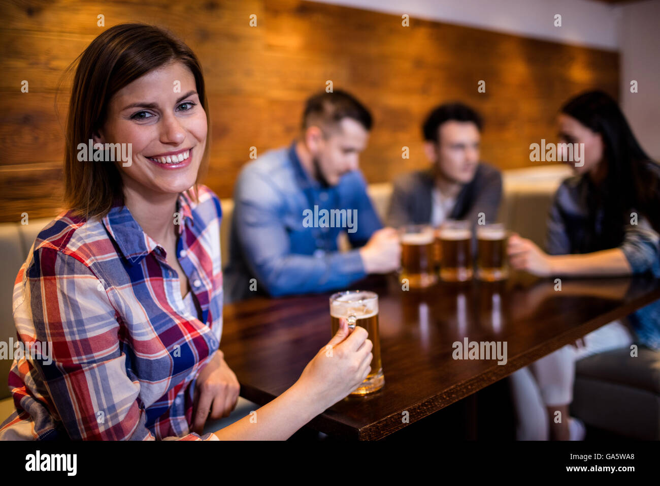 Donna che mantiene boccale di birra con gli amici in background Foto Stock