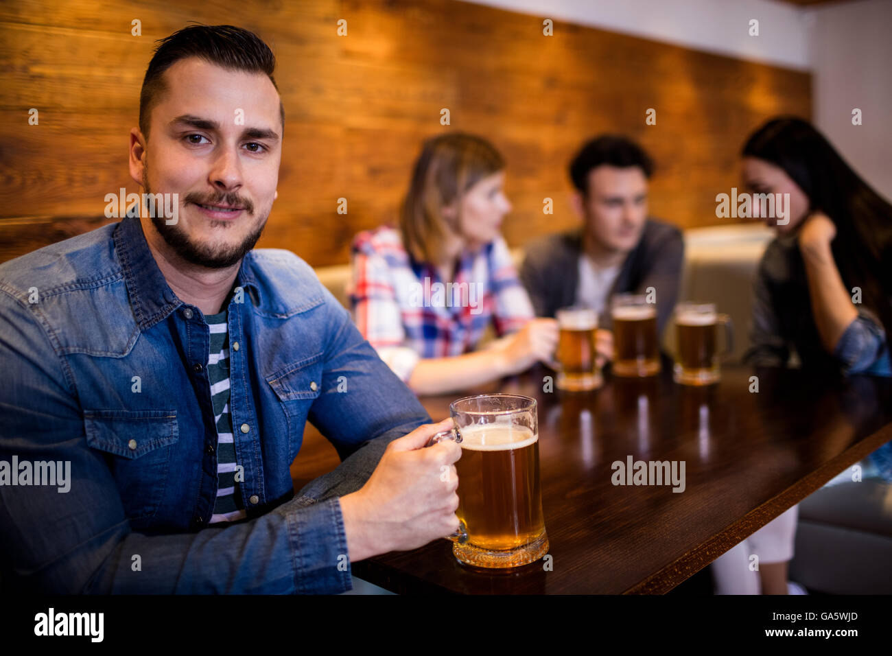 Uomo con boccale di birra mentre gli amici in background Foto Stock