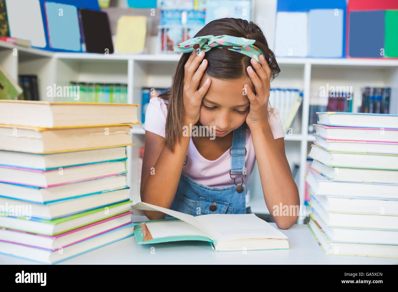 School girl leggendo un libro in biblioteca Foto Stock
