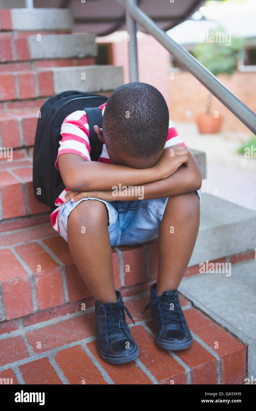 Triste schoolboy seduto da solo sulla scala Foto Stock