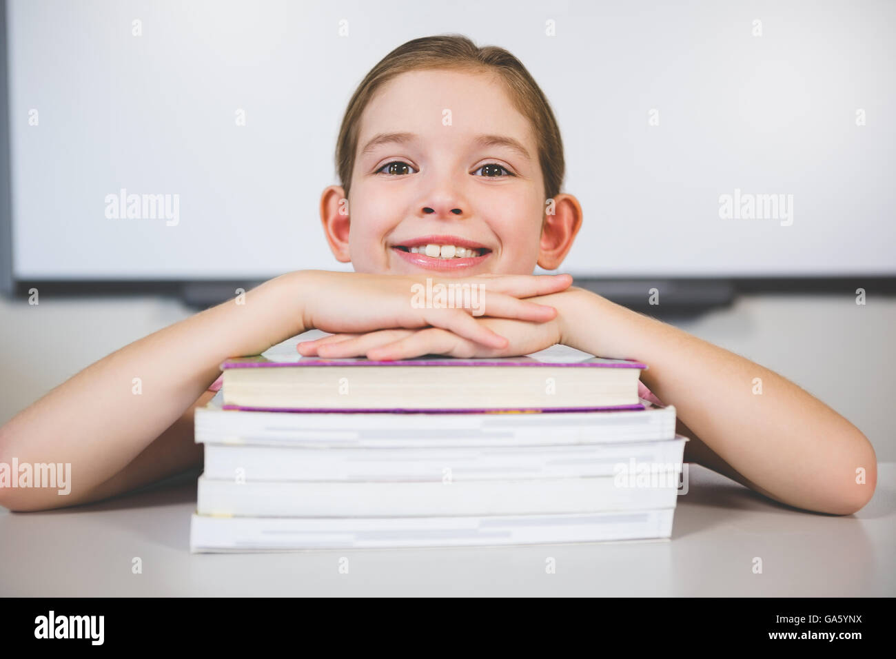 Ritratto di ragazza sorridente appoggiato sulla pila di libri in camera di classe Foto Stock