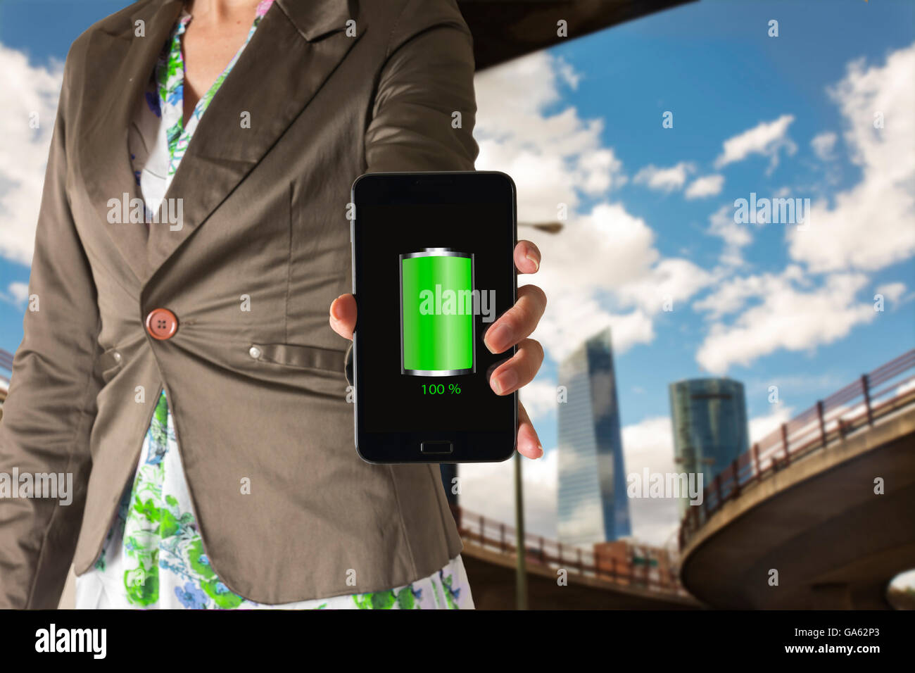 La donna che mostra un telefono cellulare con verde pieno icona della batteria nella schermata, con la città dietro Foto Stock