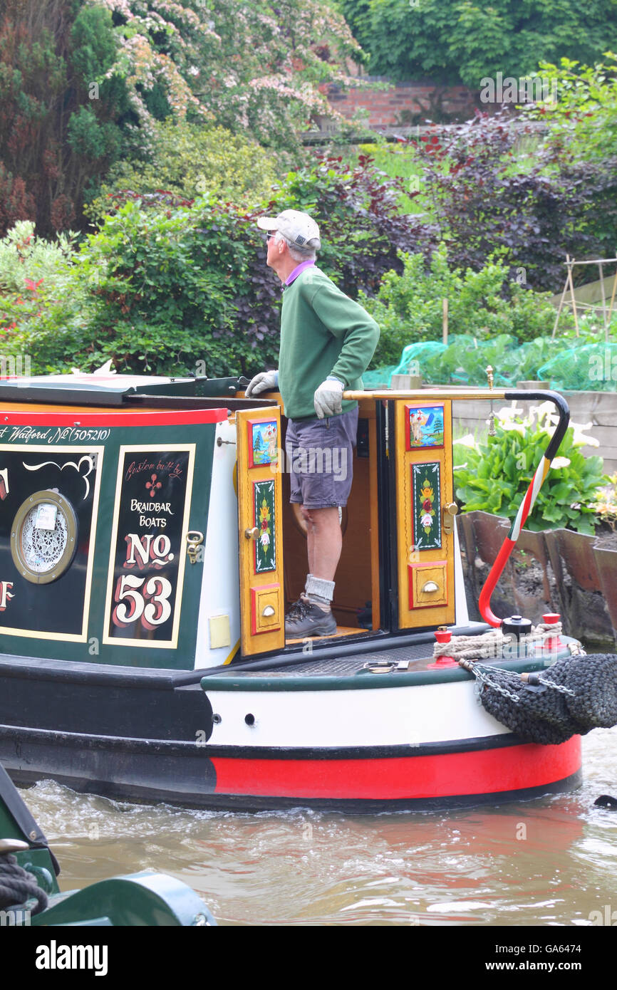 Uomo di mezza età un pilotaggio narrowboat sui Trent e Mersey Canal, vicino a Northwich, Cheshire, Inghilterra. Foto Stock