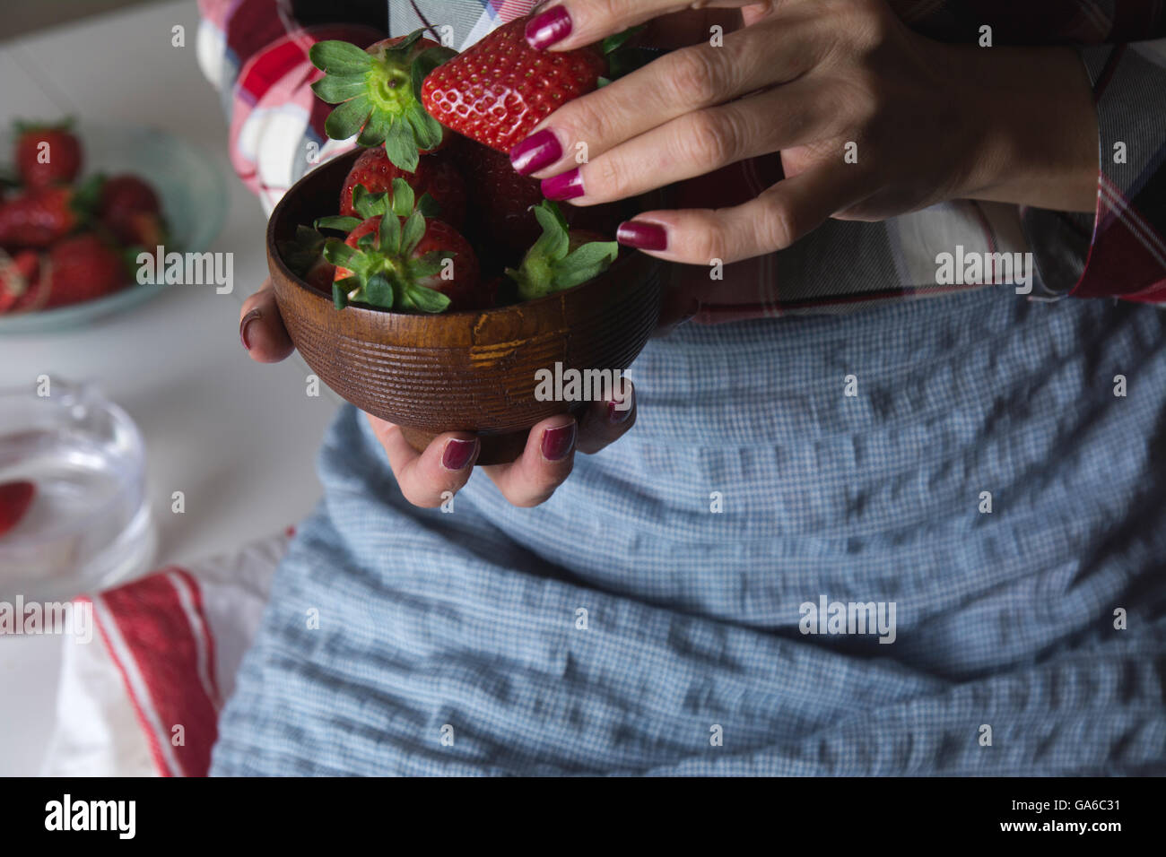 Coppa di fragole nelle mani di una donna con grembiule, seduti a tavola Foto Stock