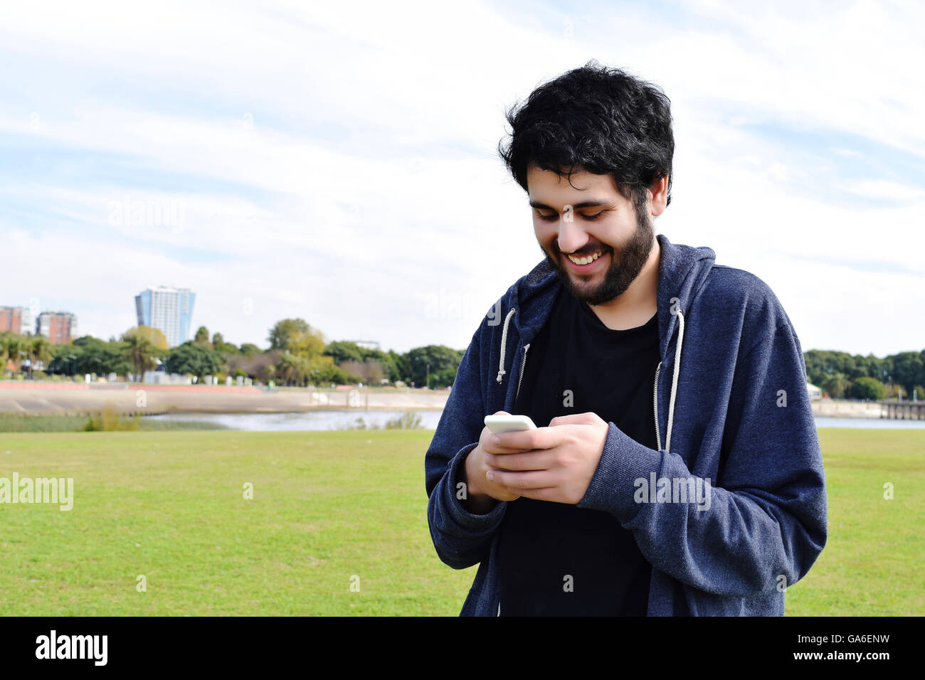 Casual giovane uomo ispanico utilizzando uno smartphone, in un parco. Foto Stock