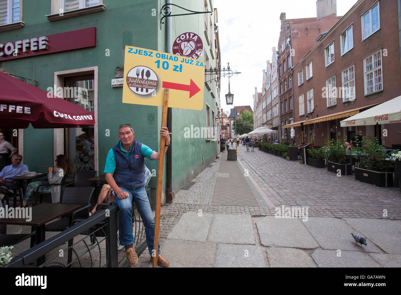 Un uomo che guarda annoiato detiene un segno advertisng un ristorante in fondo alla strada a Danzica, Polonia Foto Stock Un uomo che guarda annoiato detiene un segno advertisng un ristorante in fondo alla strada a Danzica, Polonia Foto Stock