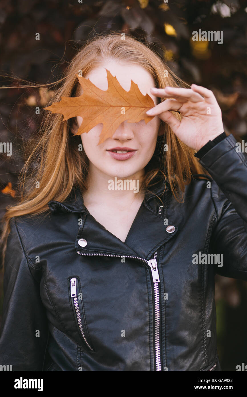 Ritratto di una ragazza redhead che coprono gli occhi con foglie di autunno Foto Stock