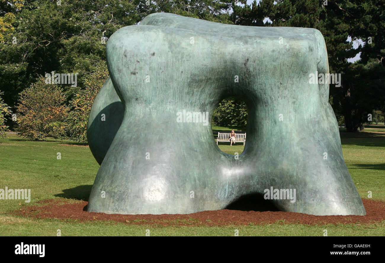 Una donna si siede su una panchina guardando una scultura di Henry Moore chiamata Large Two Forms al Kew Gardens di Londra. Foto Stock