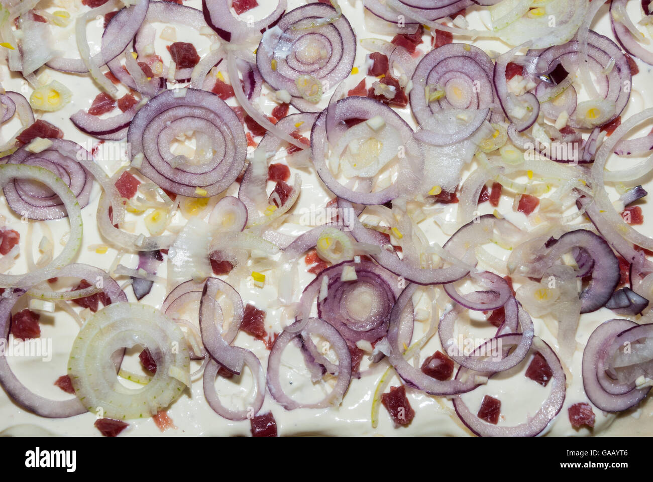 La preparazione di un piatto alsaziano, tarte flambée con panna acida, prosciutto, lardons e cipolle rosse Foto Stock