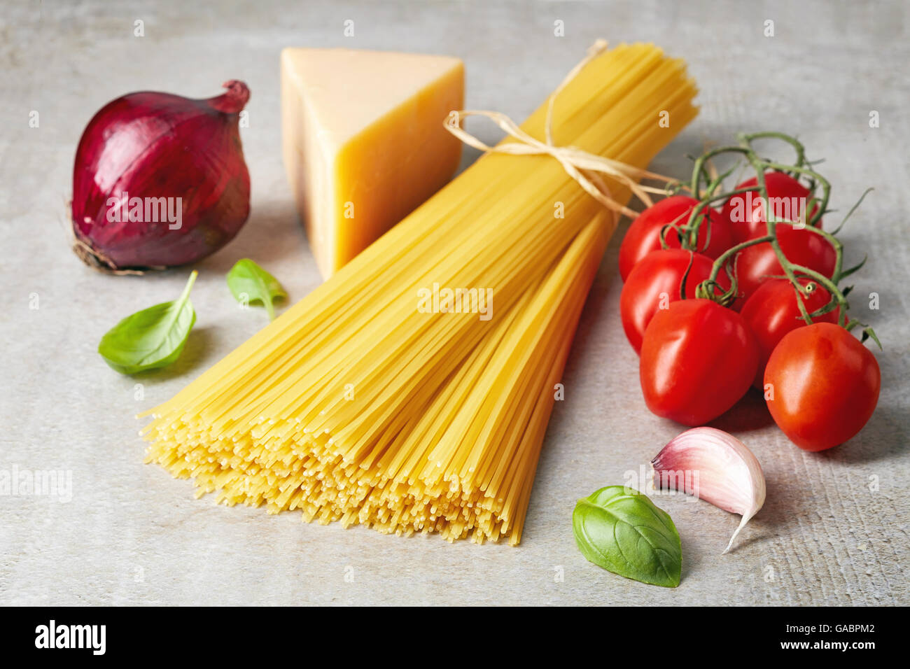 Spaghetti pomodoro, formaggio, cipolla, aglio e le foglie di basilico sulla pietra grigia tabella Foto Stock